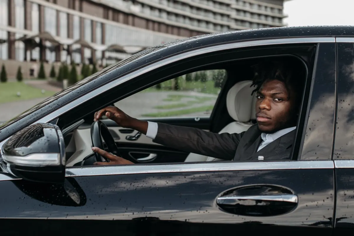 Professional driver in a dark suit at the wheel of a black executive car