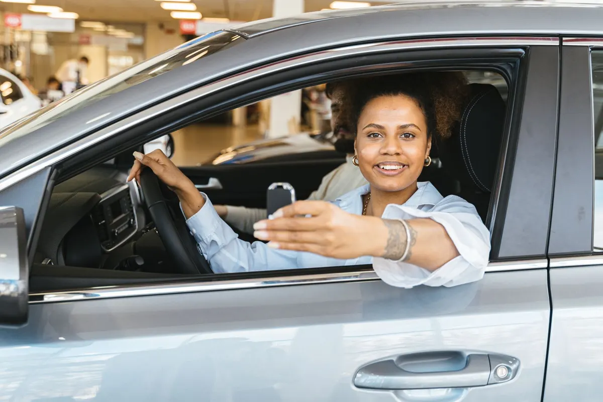 Smiling woman in the driver’s seat of a silver car, holding out the car key